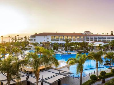 Großes Hotelresort mit mehreren Pools, Palmen und Sonnenuntergang am Horizont.