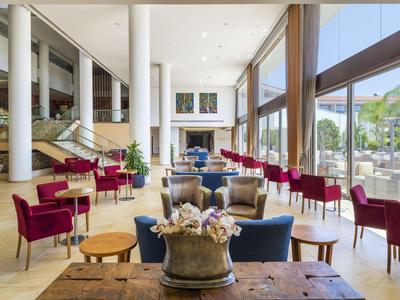 Helles Hotelrestaurant mit großen Fenstern, roten Sesseln und eleganter Einrichtung.