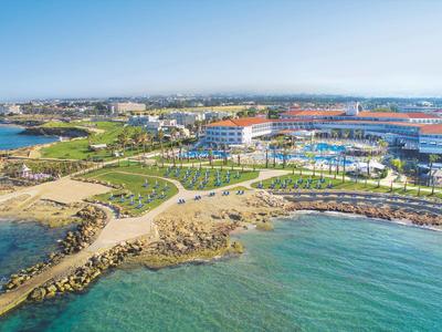 Küstenlandschaft mit Sandstränden, grünen Flächen und Gebäuden am Meer unter klarem Himmel.