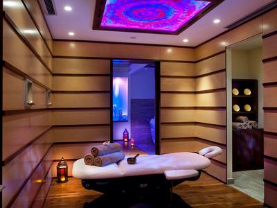 Moderner Wellnessraum mit bequemer Liege, Holzverkleidung und buntem Deckendisplay.