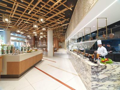 Moderner Restaurant-Innenraum mit Holzgitter-Decke, Marmor-Theke und Koch in weißer Kleidung.