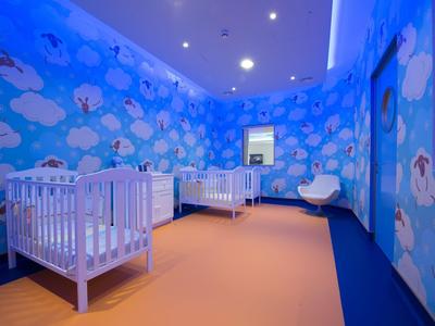 Kindergartenraum mit blauen Wänden, weißen Wolken, 3 Gitterbetten und hellorangefarbenem Boden.