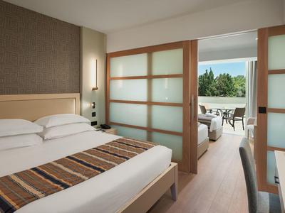 Nowoczesny pokój hotelowy z łóżkiem podwójnym, przesuwnymi drzwiami i dostępem do tarasu z widokiem na ogród.