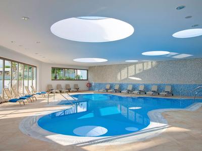 Nowoczesny kryty basen z okrągłym jacuzzi i miejscami do siedzenia w jasnym pomieszczeniu.