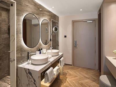 Nowoczesna łazienka z dwoma okrągłymi lustrami, umywalkami i drewnianą podłogą w pokoju hotelowym.
