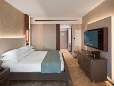 Nowoczesny pokój hotelowy z łóżkiem podwójnym, telewizorem i stolikiem nocnym.