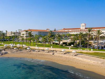 Ośrodek hotelowy nad morzem z piaszczystą plażą, palmami i parasolami pod niebieskim niebem.