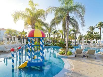 Basen hotelowy z placem zabaw wodnym i palmami pod czystym niebem.