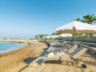 Strand mit Sonnenliegen, Sonnenschirm, palmen und blauem Himmel am Meer bei sonnigem Wetter.