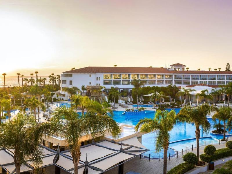 Große Hotelanlage mit Pool, Palmen und Sonnenschirmen bei Sonnenuntergang.