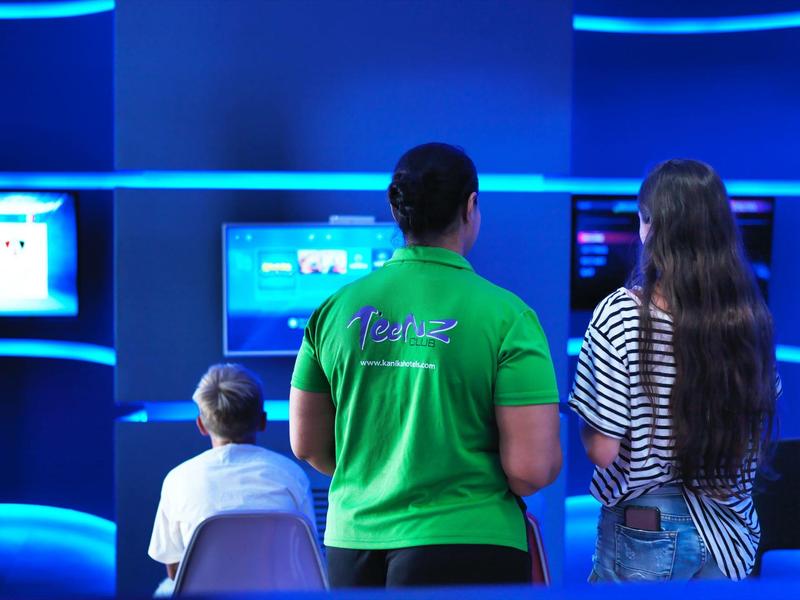 Drei Personen vor beleuchteten Bildschirmen in blauem Licht mit grüner und gestreifter Kleidung.