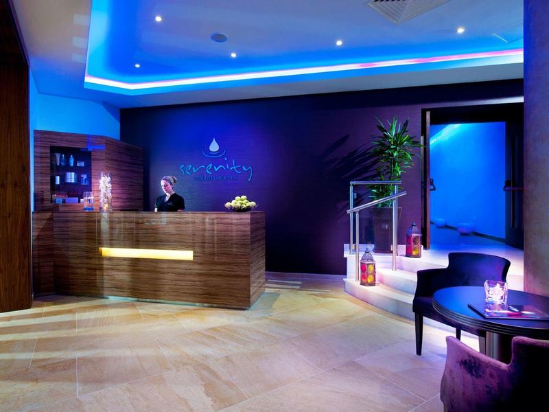 Moderne Hotellobby mit beleuchtetem Empfangstresen, violetten Wänden und gemütlichen Sitzplätzen.