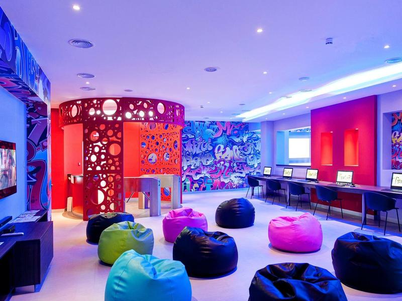 Bunt gestalteter Raum mit Sitzsäcken, Computern an Tischen und leuchtender Deckenbeleuchtung.