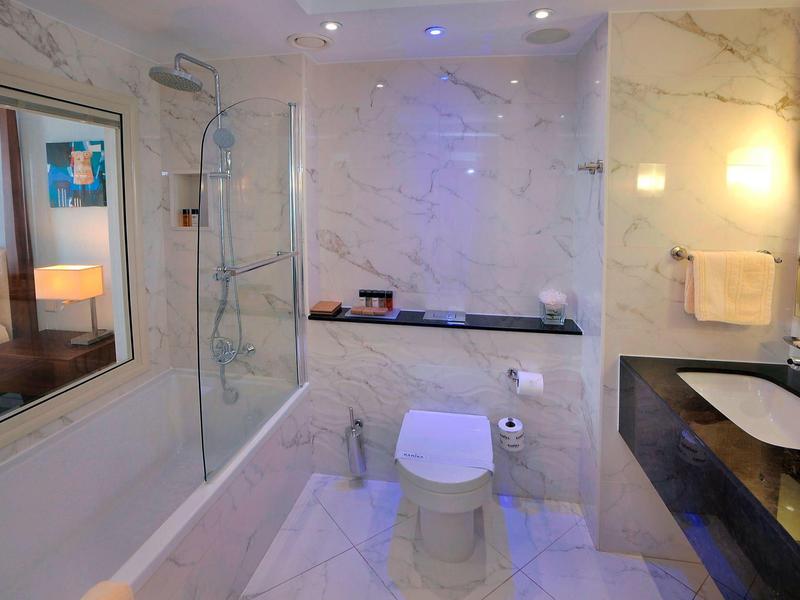 Modernes Badezimmer mit Marmorwänden, Dusche links, Toilette mittig und schwarzer Waschtisch rechts.