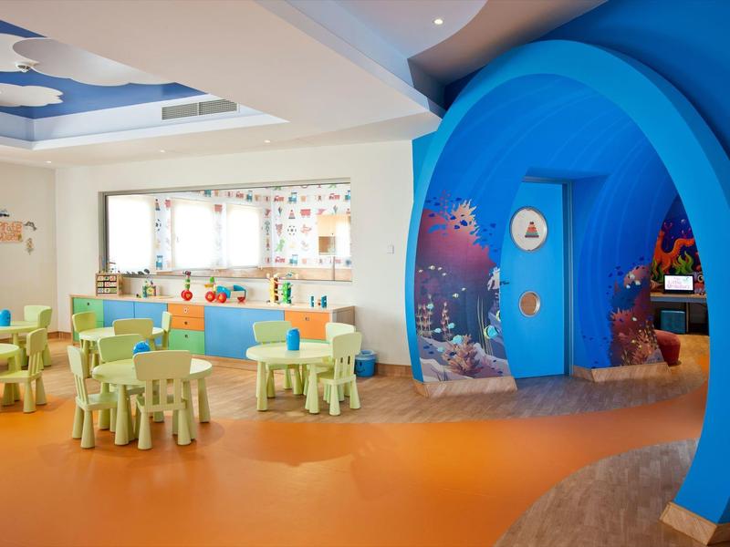 Bunter Kinderraum mit kleinen Tischen und blauem Meeresthema-Eingang linke Seite Fenster.