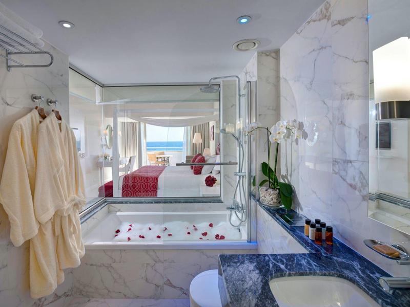 Luxuriöses Badezimmer mit Marmorwänden, Badewanne, weißem Handtuch, Orchideen und Meerblick.