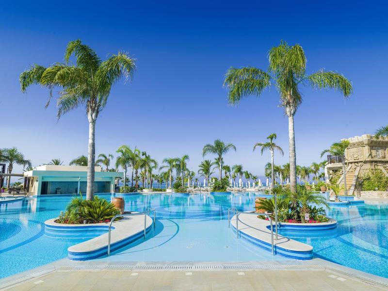 Großer Außenpool mit Inseln, Palmen und klarem blauem Himmel im Hintergrund.