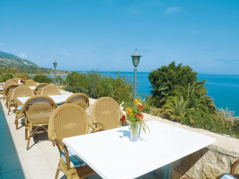 Terrassenmöglichkeit mit weißen Tischen und Stühlen vor blauem Meer und klarem Himmel.