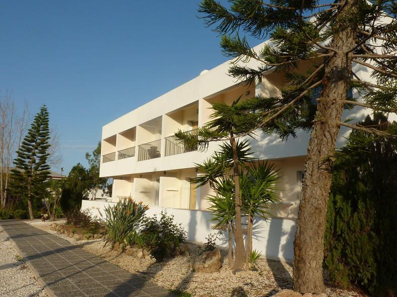 Moderner weißer Gebäudekomplex mit Balkonen an einem sonnigen Tag und Bäumen im Vordergrund.