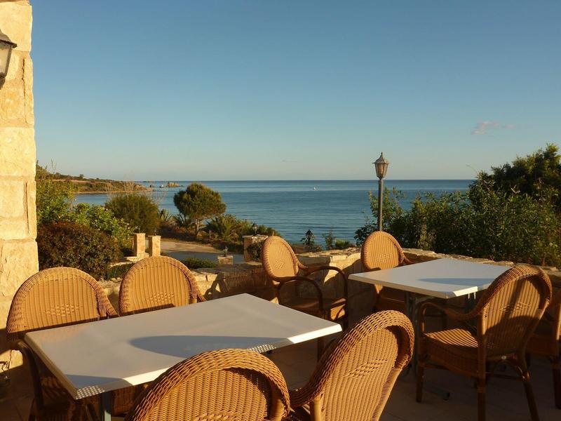 Leere Terrasse mit Tischen und Stühlen aus Korbgeflecht, Blick auf Meer und klares Blau des Himmels.