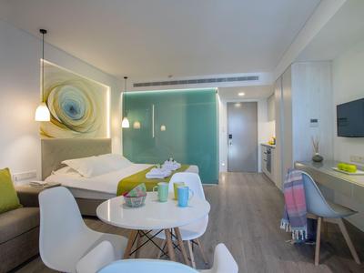 Modern hotel room with double bed, seating area, desk, and stylish lighting fixtures.