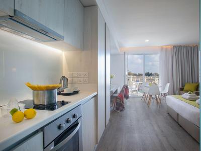 Modern hotel room with kitchenette and seating area overlooking a window.