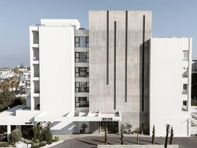 Modern white hotel building with clean lines and a wooded background.