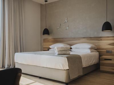 Modern hotel room with double bed, wooden wall, and two black pendant lamps.