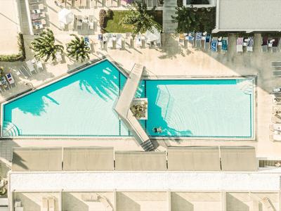 Two rectangular pools with blue water, surrounded by lounge chairs and plants at a hotel.