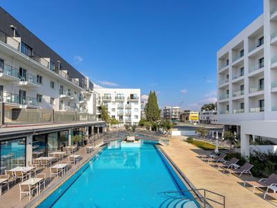 Modern hotel with large outdoor pool and sun terrace under a blue sky.