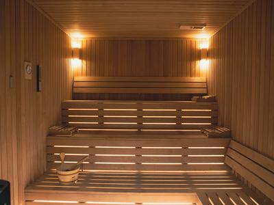 Wooden sauna with multi-level benches, warm lighting, and a sauna bucket at the lower area.