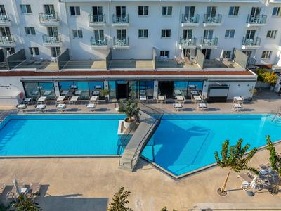 Two swimming pools in front of a white hotel with sun loungers and a connecting walkway.