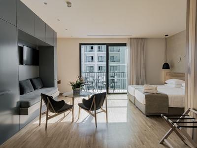 Modern hotel room with large bed, balcony, and cozy seating area.