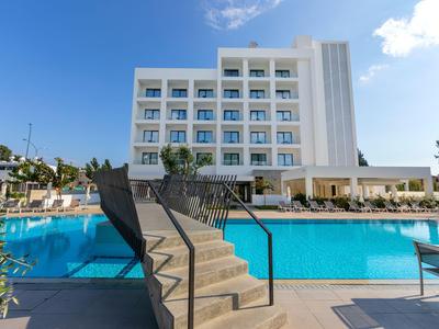 Modern hotel complex with outdoor pool, lounge chairs, and landscaped surroundings under a blue sky.