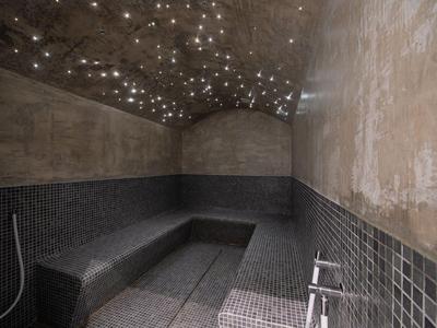 Modern steam room with black mosaic tiles and starry ceiling lighting.