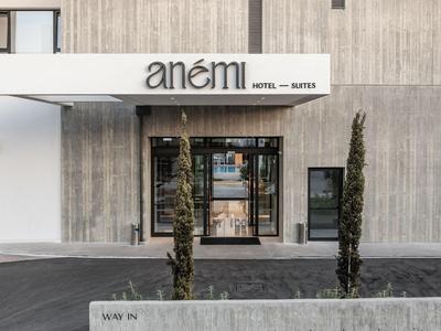 Entrance of Anemi Hotel with glass facade and minimalist gray and white design.