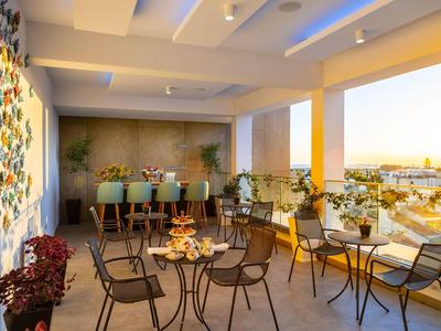 Hotel terrace with tables, chairs, and a bar illuminated by soft evening light.