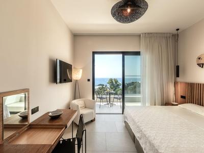 Bright hotel room with double bed, desk, chair, and balcony with sea view.