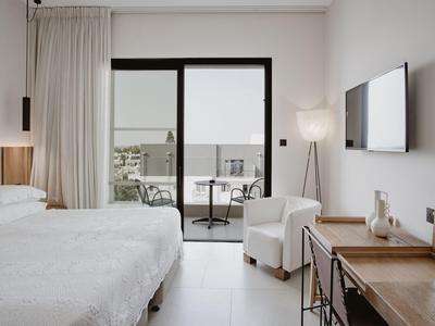 Modern hotel room with double bed, desk, chair, and balcony overlooking courtyard.