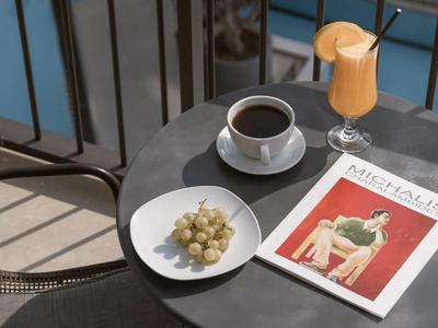Round table with coffee, orange juice, grapes, and magazine on balcony overlooking pool.