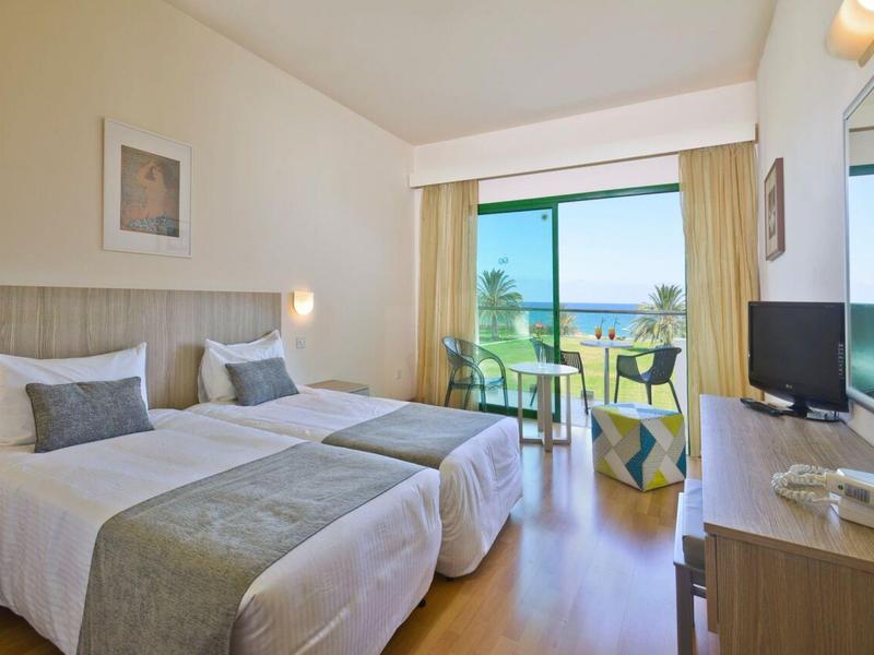 Helles Hotelzimmer mit zwei Einzelbetten, Balkon, Meerblick und Holzfußboden.