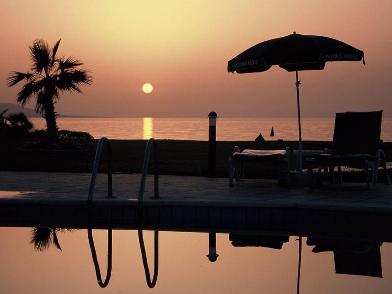 Sonnenuntergang am Pool mit Liegestuhl, Sonnenschirm, Palme und ruhigem Meer im Hintergrund.