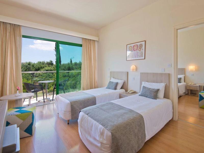 Helles Schlafzimmer mit zwei Einzelbetten, Balkon und Blick in einen grünen Garten.