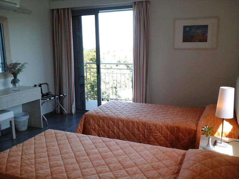 Hell eingerichtetes Schlafzimmer mit zwei Einzelbetten, orange Bettdecken und Balkon mit Blick nach draußen.