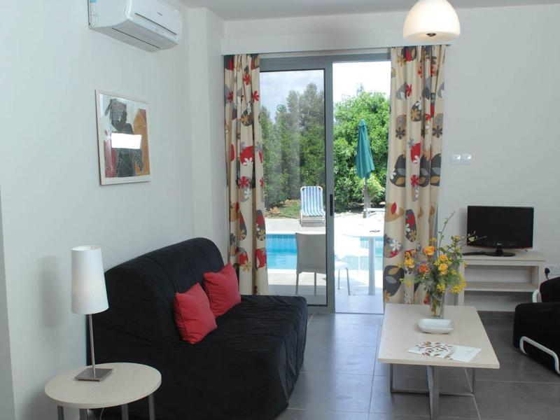 Moderner Wohnraum mit schwarzem Sofa, weißen Tischen, Fliesenboden und Blick auf Terrasse mit Pool.