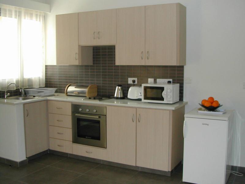 Moderne helle Küche mit Holzschränken, grauer Arbeitsplatte, weißen Geräten und orangefarbenen Früchten.