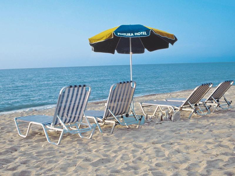 Leere Liegestühle mit blau-gelbem Sonnenschirm stehen auf sandigem Strand am ruhigen Meer.