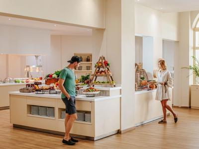 Ein heller Raum mit Buffet, zwei Personen wählen Speisen aus, moderne Ausstattung, Holzfußboden.