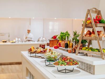 Buffet mit frischem Gemüse, Broten und Kräutern auf weißer Arbeitsfläche in modernem Raum.
