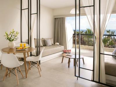 Helles Wohnzimmer mit gemütlicher Sitzecke, weißen Stühlen und großem Fenster mit Blick ins Grüne.